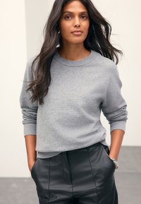 Gray sweater with ribbed cuffs and neckline, paired with black leather pants. Smooth texture, casual fit, and minimalist design details.