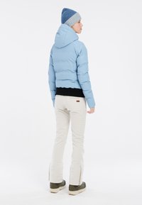 Lichtblauwe cropped pufferjack met capuchon, gecombineerd met een zwart top en witte broek met zijritsen; model draagt een blauwe gebreide muts.