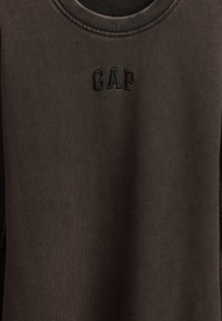 Rudas džemperis su apvalia iškirpte. Ant liemens siuvinėtas juodas „GAP“ logotipas. Audinys turi lygų paviršių ir šiek tiek blizgesio.