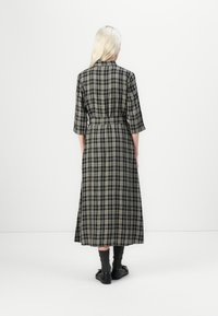 Pikk ruuduline kleit mustas ja rohelises toonis, vöökohaga, kolmeveerandi varrukatega ja voolava alläärega. Näidatud tagant.