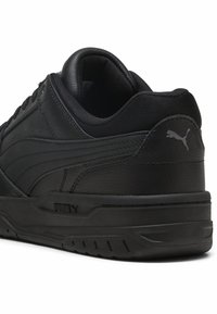 Zapatillas deportivas de cuero negro con parte superior texturizada, cuello acolchado y suela de goma. Presenta el logotipo de Puma en gris en el talón y en el lateral.