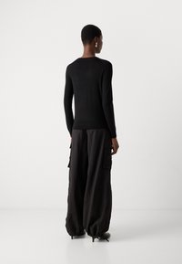 Μαύρη μακρυμάνικη μπλούζα με εφαρμοστό σχέδιο, σε συνδυασμό με άνετες μαύρες cargo παντελόνες με πλαϊνές τσέπες και στενές μανσέτες.