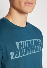 Türkises Baumwoll-T-Shirt mit großem, geometrischen "HUMMEL"-Logo in Hellblau. Klassisches Rundhals-Design mit kurzen Ärmeln.