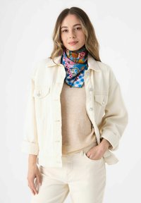 Crème denimjack over een beige sweater, gecombineerd met crèmekleurige broek. Kleurrijke sjaal met blauwe, roze en paisleypatronen om de nek.