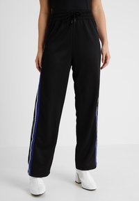 Svarta joggingsbyxor med resårmidja, som har vita och blå sidostreck. Tyget verkar vara slätt och ger en avslappnad passform.