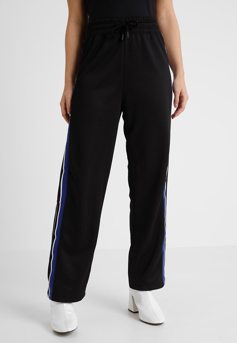 Svarta joggingsbyxor med resårmidja, som har vita och blå sidostreck. Tyget verkar vara slätt och ger en avslappnad passform.