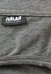 Grijs stof met een soepele textuur, met een gestikte zoom. Een zwart label met de tekst "IUMAN intimissimi uomo" staat aan de rand van de stof.