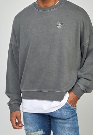 Grijze sweatshirt met een ontspannen pasvorm, ribgebreide manchetten en kraag; gekenmerkt door een klein geborduurd logo op de borst; gecombineerd met een witte onderhemd.