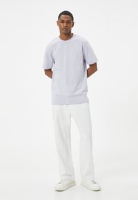 Lyserød bomulds t-shirt med rund hals og korte ærmer, parret med hvide jeans og hvide sneakers. Enkel, afslappet design.