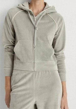 Jasnoszara bluza z kapturem na zamek błyskawiczny, z przednimi kieszeniami i ściągaczami, noszona z dopasowanymi jasnoszarymi spodniami.