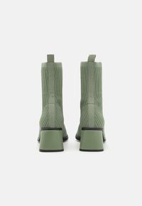 Un par de botas de tobillo de punto verdes con tacones de bloque, tiradores en la parte trasera y un patrón de ribetes verticales texturizados.