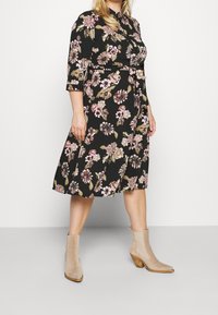 Black floral dress with three-quarter sleeves, cinched waist, knee-length skirt, featuring pink and cream flowers. Beige ankle boots with a block heel.