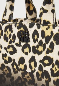 Sac fourre-tout en imprimé léopard fabriqué en tissu texturé ; dispose de poignées noires et d'un logo DKNY noir bien en vue.