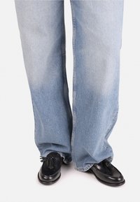Wijde lichtblauwe jeans met een vervaagde textuur, gecombineerd met zwarte leren loafers met kwastaccenten.