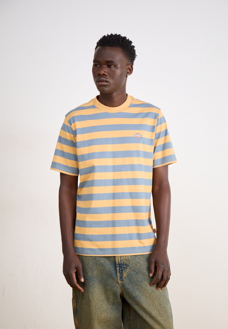 Camiseta a rayas con colores azul y amarillo, de mangas cortas, escote redondo y un pequeño logo en el pecho. Hecha de tela de algodón.