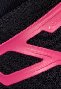 GORE-TEX® svart tyg med en texturerad yta, med en framträdande rosa plastdetalj i zigzagform.