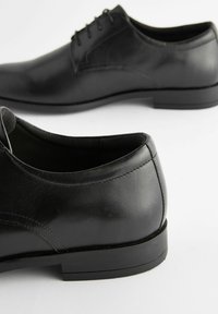Zapatos de vestir de cuero negro con punta redondeada, acabado suave, cordones de cinco ojales y suela plana de goma baja.