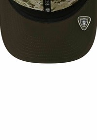 Schwarze Baseballkappe mit flachem Schirm, ausgestattet mit einem Raiders-Logopatch und einem Innenfutter im Camouflage-Muster. Genähte Details entlang des Schirms.