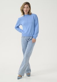 Ljust blått stickat tröja med hög krage, puffärmar och ribbat fåll. Matchas med ljusblå utsvängda jeans och matchande klackar.