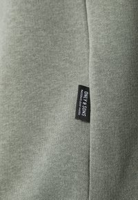 Primo piano di un tessuto verde con un'etichetta nera con la scritta "ONLY & SONS" cucita in una cucitura sul lato destro.