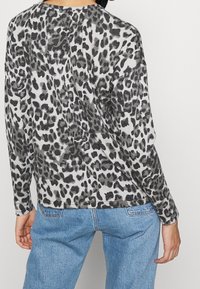 Langärmliges Oberteil in Grau mit schwarzen Leopardenflecken, mit lockerer Passform, rundem Ausschnitt und weichem Material. Kombiniert mit hellblauen Jeans.