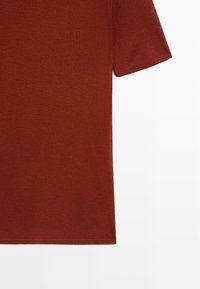 Short-sleeve crew neck t-shirt in rust color, made of smooth cotton fabric with a straight cut, featuring clean edges and no patterns.