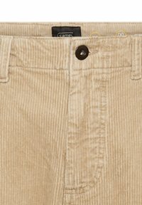 Beige corduroy pants with a textured surface, featuring a single brown button closure and a brand label visible at the waistband.
