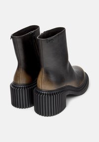 Botas de tobillo de cuero negro y marrón con suela de goma negra acanalada. Presenta un cierre de cremallera y un diseño de punta redondeada.