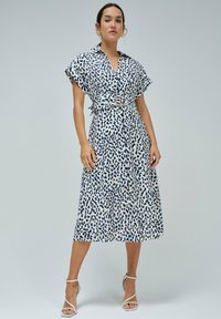 Košilové midi šaty v bílé barvě s modrým tečkovaným vzorem. Mají pásový úplet v pase a krátké rukávy. Hladká, lehká tkanina.