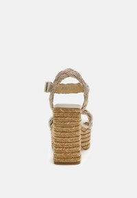 Wedge sandals with a braided natural fiber upper, beige straps, and a thick, woven platform heel. White outsole and adjustable ankle strap.