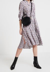 Blommig klänning i mjukt tyg, med en knäppt krage, korta puffärmar och sidofiléer. Matchas med en svart rund handväska och klackboots.