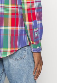 Koszula w wielokolorową kratekę, zawierająca odcienie czerwonego, zielonego, niebieskiego i żółtego. Miękki materiał z zapięciem na guziki przy mankietach i zakrzywionym dołem. W połączeniu z jasnymi dżinsami.