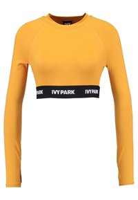 Langärmliges Crop-Top aus leuchtend gelbem Stoff mit taillierter Passform, ausgestattet mit einem schwarzen elastischen Band mit der Aufschrift "IVY PARK" an der Taille.