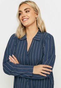 Camicia blu navy con bottoni, a righe verticali bianche, in cotone, maniche lunghe e colletto. Ha una vestibilità comoda.