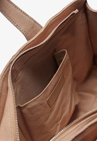 Borsa tote in suede beige con chiusura a zip, tasca interna e texture liscia. Presenta un design minimalista con dettagli di cucitura discreti.