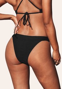 Ensemble de bikini noir comprenant un bas taille haute texturé et un haut à nouer au dos avec des bretelles réglables. Design simple et monochrome.