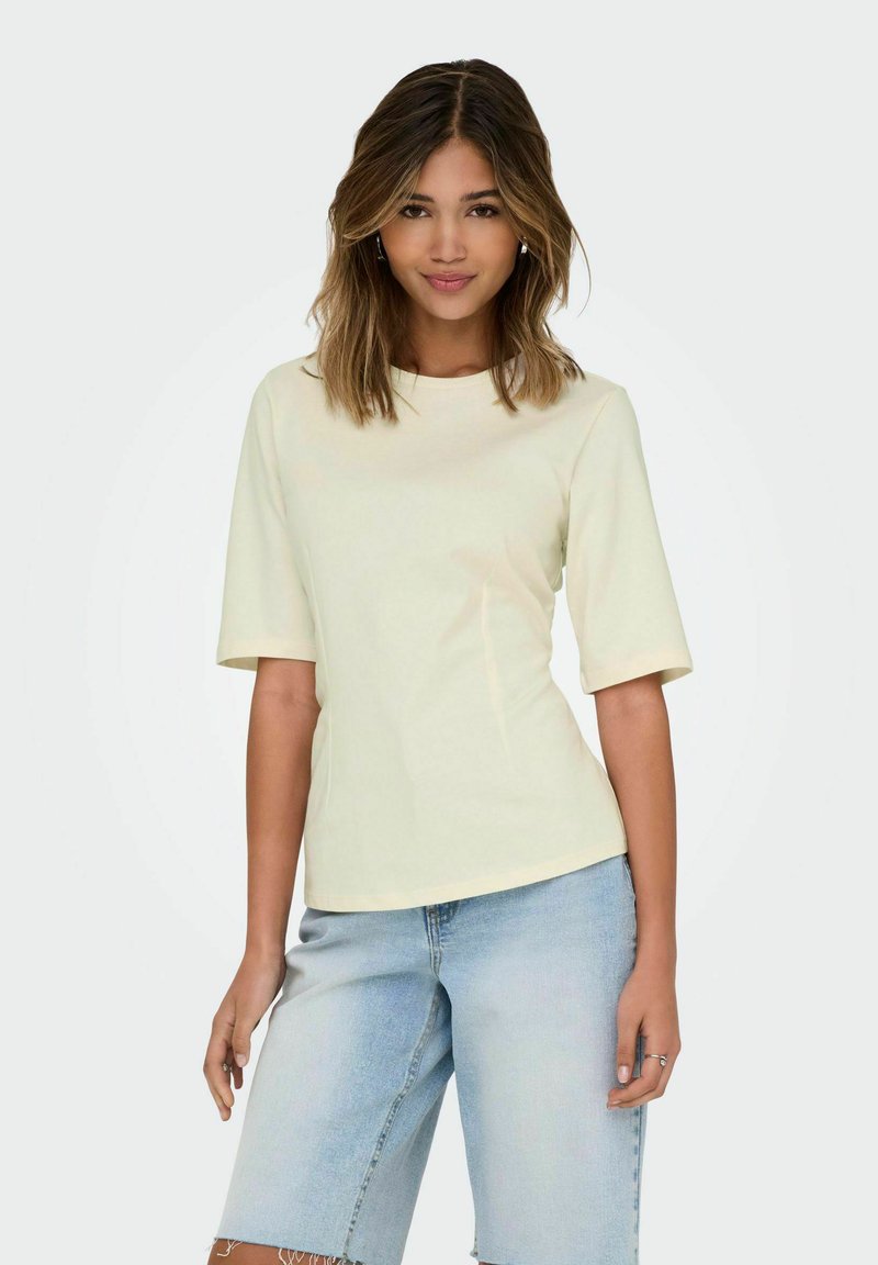 Haut jaune clair à manches courtes avec un col rond, associé à un short en denim bleu clair présentant des bords effilochés.
