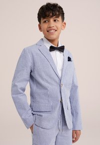 Costume rayé en bleu clair et blanc, avec une veste à un seul bouton ornée de boutons en or, une chemise blanche et un nœud papillon noir.