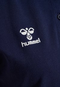 Marineblå polo-shirt med et tekstureret stof. Indeholder en hvid logo bestående af en stiliseret bi og teksten "hummel" nedenunder.