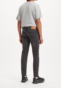 Grå bomulls-T-shirt kombinerad med mörkgrå slim-fit jeans. Märkbara detaljer inkluderar ett lädermärke på baksidan och svarta sneakers med vita detaljer.