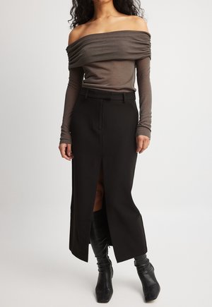 Kvinde iført en brun off-shoulder top med lange ærmer, sort midi-nederdel med høj talje og frontslids samt sorte knæhøje støvler.