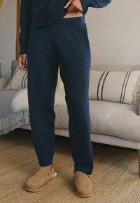 Navy knit sweatpants with a relaxed fit, featuring a soft texture and a high waistband, paired with tan slip-on shoes.