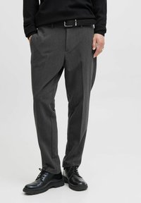 Pantalones grises ajustados con un acabado texturizado, que presentan un corte recto, pliegues frontales y un cinturón negro. Combinados con zapatos negros de cordones.