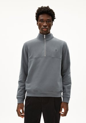 Sweatshirt gris à demi-zip fabriqué dans un matériau doux, avec un col montant, des poignets côtelés et un petit logo sur la poitrine. Design simple.