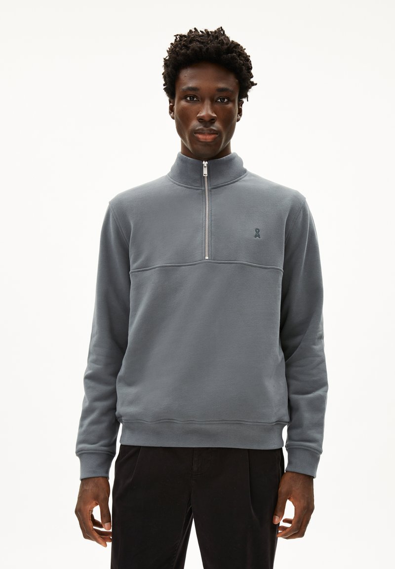 Felpa grigia a mezza zip realizzata in materiale morbido, con colletto alto, polsini a coste e un piccolo logo sul petto. Design semplice.