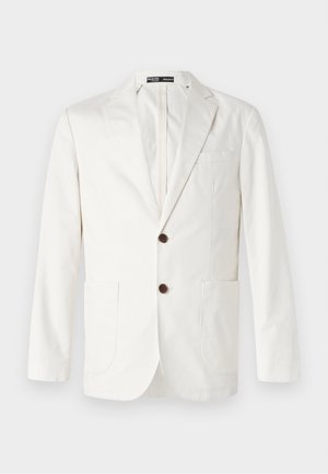 Lys beige blazer laget av bomull, med spiss krage, to frontlommer og to brune knapper for lukking.
