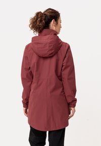 Giacca impermeabile bordeaux con cappuccio, polsini elasticizzati e taglio dritto. Tessuto liscio e dettagli minimali.