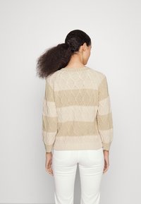 Maglione a maglia con un motivo geometrico in beige e nocciola chiaro. Presenta maniche a tre quarti e orlo a costine. La texture appare morbida e traspirante.