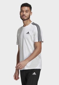 Witte katoenen T-shirt met zwart adidas-logo op de linkerkant van de borst, met drie zwarte strepen op elke schouder, ronde halslijn, ontspannen pasvorm.