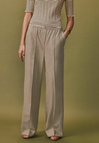 Lichtbeige hoge taille broeken met een zachte, gestructureerde afwerking, voorzien van voorplooien en zijzakken, gecombineerd met een gestreepte top.